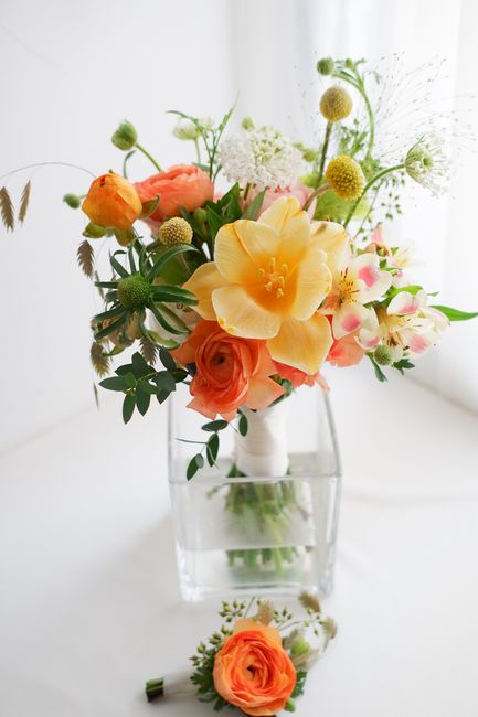 A vibrant bouquet of fresh flowers arranged in a white vase, featuring large yellow amaryllis, soft peach roses, and delicate pink and white blossoms, complemented by green foliage and small white and