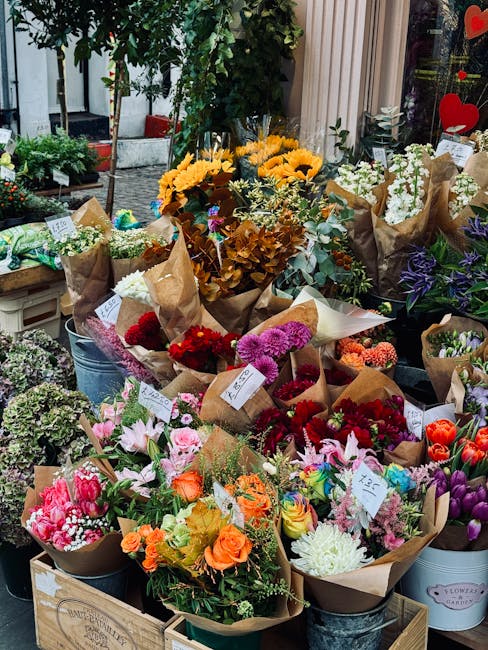A vibrant display of fresh flowers arranged in bouquets at a flower shop, featuring a variety of blooms including bright yellow sunflowers, pink lilies, red roses, purple irises, and white chrysanthem