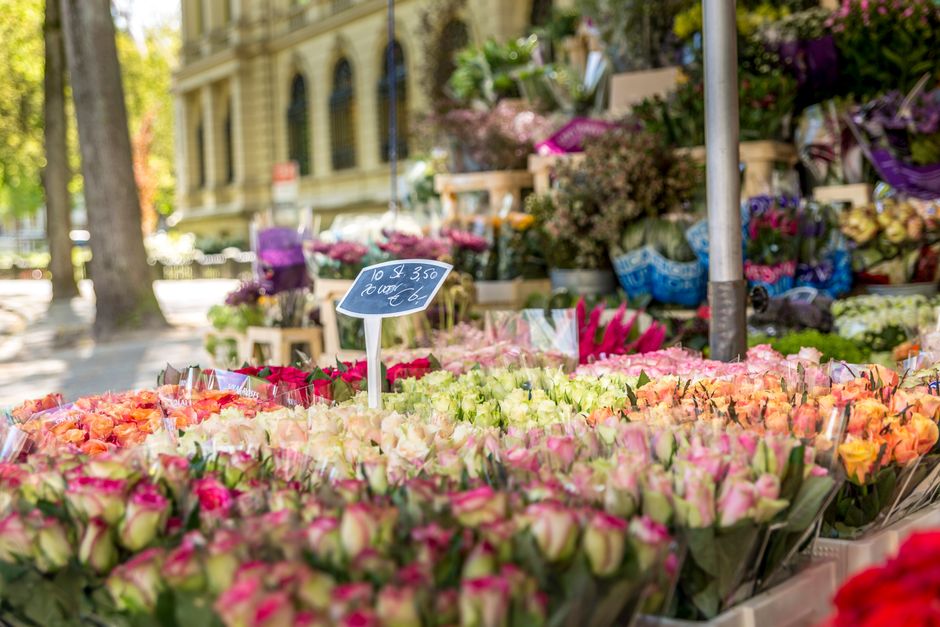 A vibrant outdoor market stall displaying an extensive selection of fresh flower bouquets. The flowers include pink and cream roses, peach-colored roses, and delicate white blossoms, arranged in neat