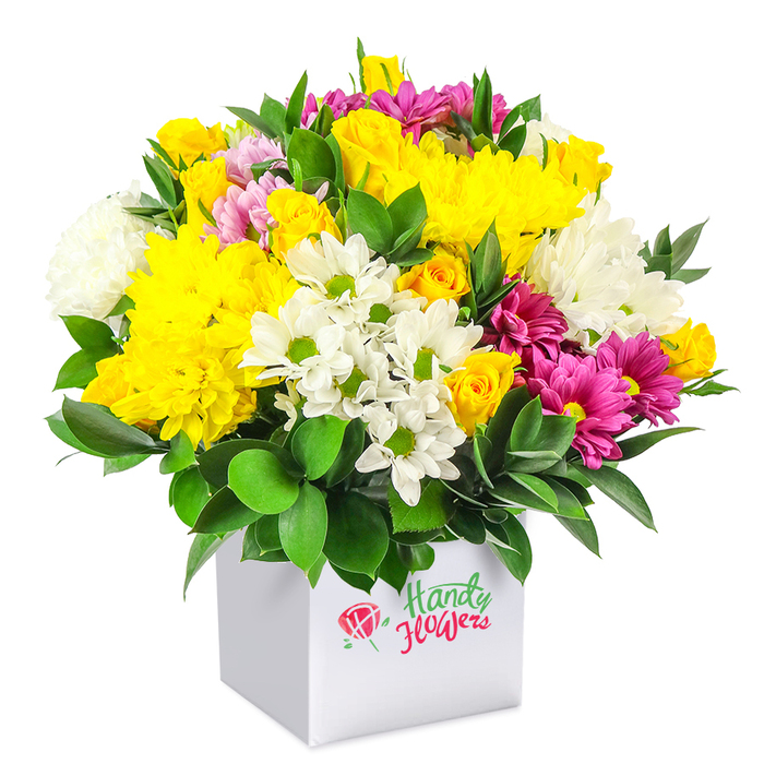 A compact yet luxurious bouquet of mixed flowers in bright yellow, crisp white, and rich fuchsia tones rises from a contemporary white square box, all set against a white background that allows the colours and shapes to take centre stage. The blooms are arranged in a smooth, rounded dome, packed so generously that the flowers press gently against one another, forming a seamless tapestry of petals. At the centre, golden yellow chrysanthemums and tightly budded spray roses provide a warm glow, their soft, layered petals catching the light and echoing the cheerful bustle of Lower Clapton's local markets. Scattered through this sunny heart are white daisy-style chrysanthemums with green centres and larger white mums, whose clean lines and fluffy textures bring a cooling, cloud-like counterpoint. Fuchsia and magenta chrysanthemums curl through the design, some petals deep and saturated, others brushed with lighter pink, creating depth and a touch of romantic flair. Dark green, polished foliage shapes the base of the arrangement and pushes up between stems, adding definition and a refreshing, garden-like quality, as if gathered near the paths of Millfields Park. The square box itself is minimalist and bright, its flat surfaces presenting the flowers as a carefully wrapped gift, easy to carry up a stairwell or set on a café counter. Flower Delivery Lower Clapton might present an arrangement like this as an accessible yet impressive option for birthdays, quick thank-you gestures, or to brighten a new flat. The bouquet's visual story is one of optimism and everyday celebration, with every petal placed to create a sense of abundance without feeling fussy or overworked.