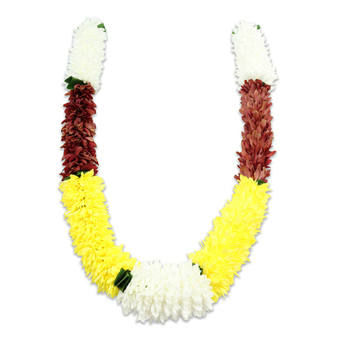 A richly hued, U-shaped mala-style garland lies against a pure white background, the lighting arranged to show the dense construction and the soft shadow that gives it dimensionality. Each arm begins with thick, cylindrical sections of creamy white fabric blooms-fluffy, compact and airy in impression-then moves into an intense maroon band of similarly textured, small petals that add depth and warmth. The longest stretch of each arm is a generous field of bright yellow flowers, executed with a plush density that creates the garland's sweeping curve. At the bottom centre, where the yellow arcs meet, a substantial cluster of pristine white chrysanthemum-like blooms forms a striking focal knot, while tiny dark green leaf-like separators mark the transitions and lend a natural counterpoint to the vivid colour blocks. Close inspection reveals meticulous hand-assembly: layers of individual fabric petals stitched and arranged to achieve a full, consistent volume-an approach favoured for garlands used repeatedly in religious ceremonies, weddings, or festival decorations because it preserves shape and colour. The overall effect is traditional and celebratory at once, the palette carrying symbolic notes of purity, prosperity and devotion. Locally, this style of garland is often chosen by families preparing for puja or festive gatherings around Chatsworth Road Market, Clissold Park and the neighbourhoods that converge in Lower Clapton, where cultural traditions and careful floral craft meet.