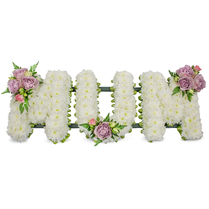 An elegant, traditional funeral tribute spelling MUM, crafted from hundreds of pristine white chrysanthemums densely packed to form each letter with a soft, uniform texture that suggests clouds or freshly fallen snow. The white backdrop and even lighting allow the subtle sculptural work to show through: each M and the central U are modelled with a tactile, rounded surface that invites a gentle touch and reads as a calm, reverent presence. Three modest clusters of accent blooms-pale lavender roses paired with small blush pink rosebuds and surrounded by fresh green leaves-are positioned to create a flowing rhythm across the piece: one cluster adorns the upper left arm of the first M, another sits serenely in the U's inner curve, and the third embellishes the upper right arm of the final M. Wisps of fern and lighter green foliage slip between the white chrysanthemums, adding depth, contrast, and a soft green perfume that complements the roses' velvety scent. A dark green support frame, possibly ribbon-wrapped or moss-covered, is visible along the base, grounding the composition and ensuring the lettering retains a dignified, upright form. This heartfelt MUM arrangement is conceived for moments of remembrance-funerals, wakes, or graveside services-and has the measured, comforting quality of creations we prepare for families who know the peaceful corners of Lower Clapton, from Clapton Pond to the riverside paths by the Lea.