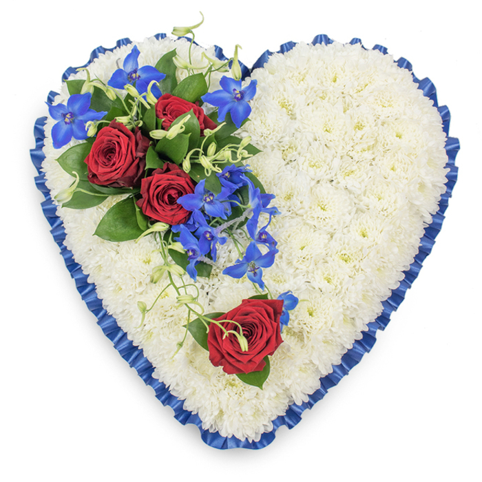 This funeral heart arrangement is captured in a clear, top-down view, making every element of its design easy to imagine. Shaped as a classic heart, the tribute is densely packed with pristine white chrysanthemums, each bloom slightly domed so that, together, they form a luxuriously padded surface. The mums create a smooth, cloud-like texture that feels calm and quietly supportive, echoing the sense of shared sympathy often felt at services in Lower Clapton's community spaces. Around the entire perimeter runs a royal blue satin ribbon, neatly pleated so that it forms a delicate, ruffled edge. The satin's sheen adds a soft glow and sharply defines the silhouette of the heart, introducing an air of formality and care. On the upper left portion of the heart, a striking focal spray brings a burst of colour and emotion. Three fully opened red roses, their velvety petals rich and layered, are nestled among deep green leaves, symbolising enduring love and devotion. Flowing from this cluster are elegant stems of electric blue dendrobium orchids, their star-shaped petals glowing with vivid blue and purple undertones as they trail over the white base. Fine, curly green tendrils thread through the roses and orchids, giving the spray a gentle, organic rhythm that contrasts beautifully with the structured edge of the ribbon. Positioned on the lower right curve of the heart sits a single red rose, carefully placed as a quiet echo of the main group, bringing visual balance and suggesting one precious life remembered. The composition feels serene, dignified, and deeply heartfelt, an ideal tribute for a funeral or memorial service in or around Lower Clapton, where families wish to express their love, respect, and remembrance with grace.