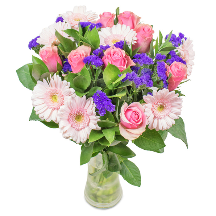 Poised in a clear glass vase against a soft, welcoming backdrop, this striking bouquet invites the eye with its intricate balance of pink and purple-a tribute to Lower Clapton's lively streets. Seven to nine roses in tender shades of pink spiral outward, some just opening, exuding both romance and refinement. Interspersed are five to seven pale pink gerbera daisies, their broad, playful faces surrounding creamy centers and echoing the spontaneous joy of local wildflower patches. Bright clusters of purple statice or limonium add dynamic colour contrast and a touch of whimsical character, much like the urban gardens tucked away behind Victorian terraces. The bouquet's enveloping greenery, deep and glossy, suggests freshness and vitality, anchoring the pinks and purples with notes of woodland scent. Stems are clearly visible in the water-filled vase, highlighting the natural integrity and expert arrangement that marks every Flower Delivery Lower Clapton creation. Suitable for celebrations big and small-from birthdays to just-because gestures-this bouquet translates the warmth and diversity of Lower Clapton directly into your home.